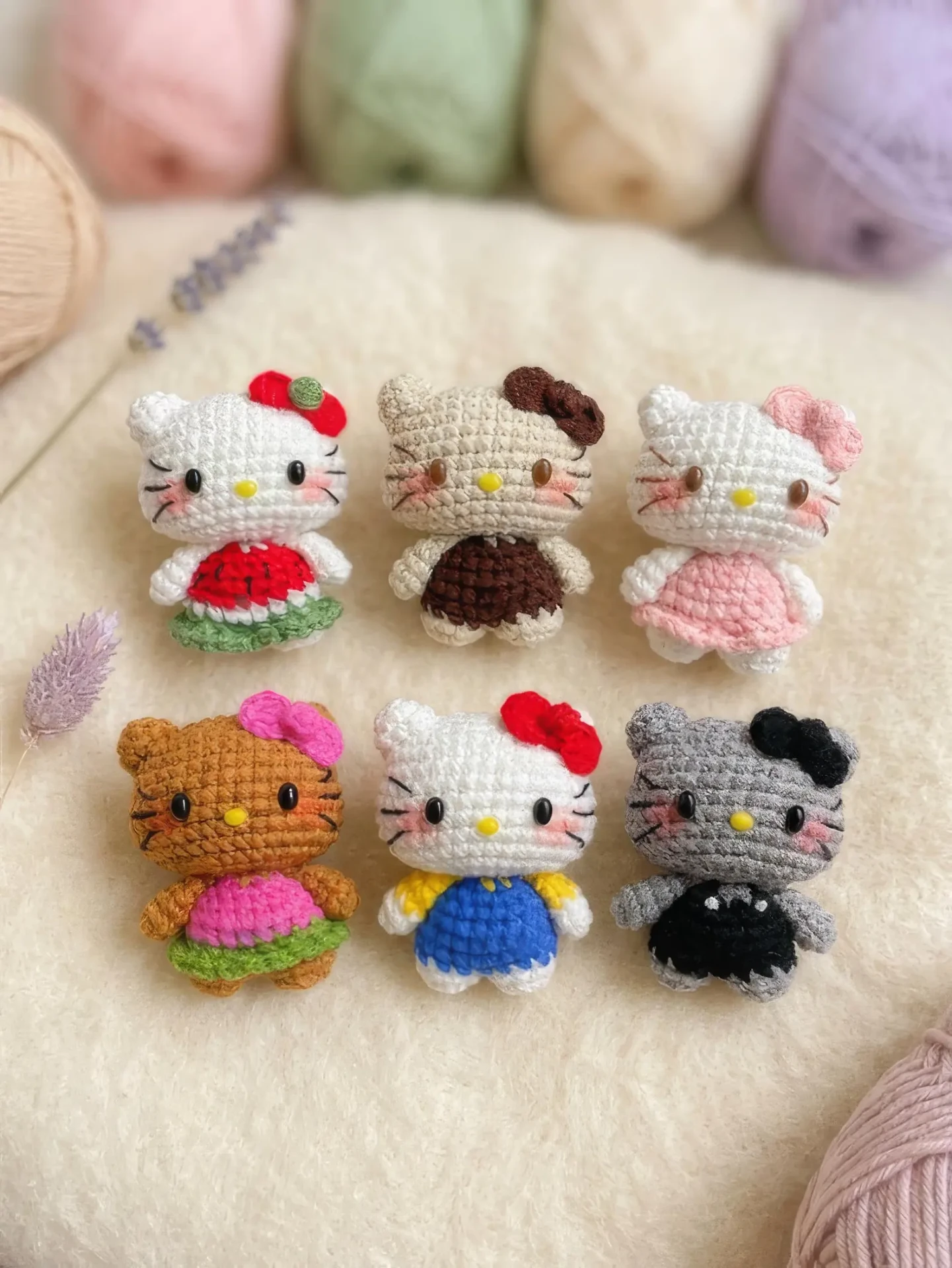 Six pastel crochet kitty keychains arranged on a blanket